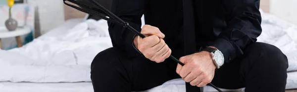 Cropped view of man with flogging whip sitting on bed, panoramic shot — Stock Photo