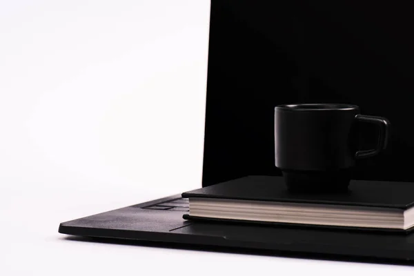 Black notebook and cup on laptop with blank screen isolated on white — Stock Photo