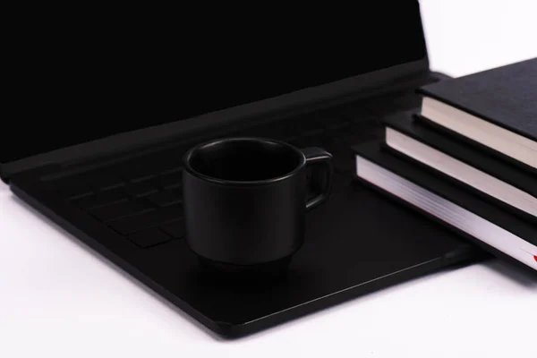Notebooks and cup near black and modern laptop isolated on white — Stock Photo
