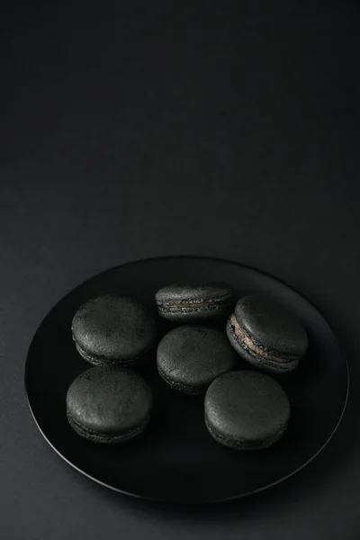 Vue de dessus de la plaque avec des macarons sombres et savoureux sur noir — Photo de stock