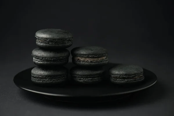 Teller mit dunklen und schmackhaften Macarons auf schwarz — Stockfoto