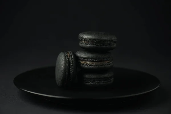 Plate with dark macarons on black with copy space — Stock Photo
