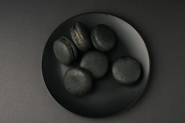 Vue de dessus de la plaque avec des macarons sombres isolés sur noir — Photo de stock