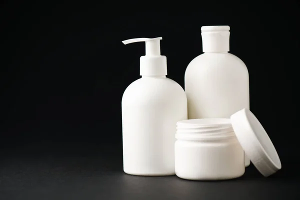 Container with face cream near white bottles on black — Stock Photo