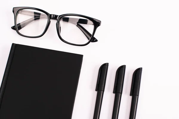 Stifte in Brillennähe und schwarzes Notizbuch isoliert auf weiß — Stockfoto