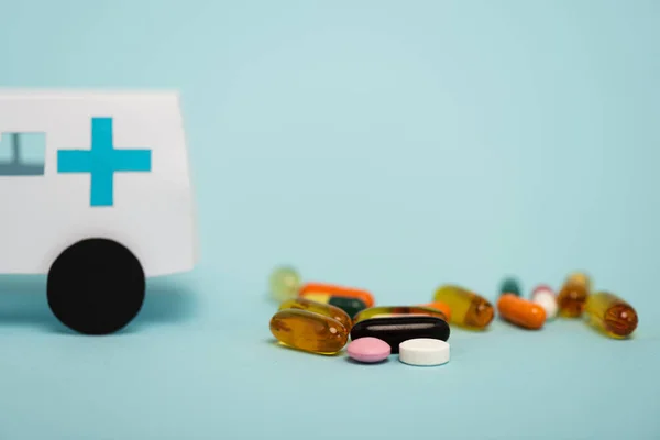 Selective focus of pills and toy ambulance car on blue background — Stock Photo