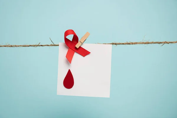 Card with blood drop and red ribbon on rope with pin isolated on blue, concept of hemophilia — Stock Photo