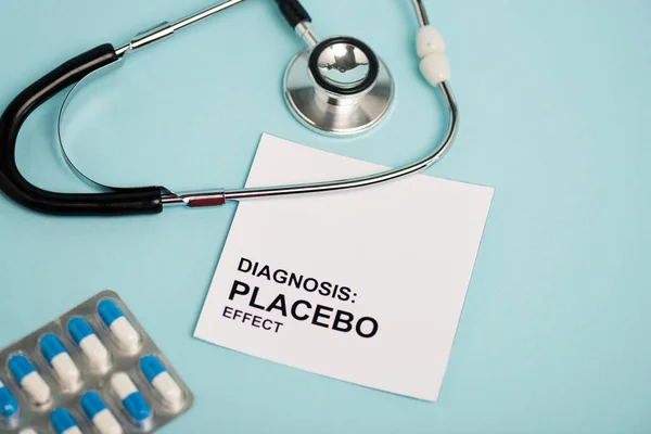 Karte mit Placeboeffekt-Schriftzug, Pillen und Stethoskop auf blauem Hintergrund — Stockfoto