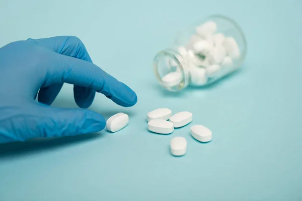 Foco seletivo do médico segurando pílula perto jar no fundo azul — Fotografia de Stock