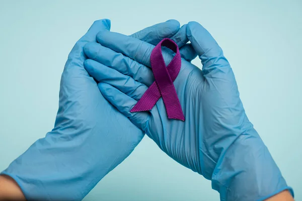 Cropped view of doctor in latex gloves holding purple ribbon isolated on blue — Stock Photo