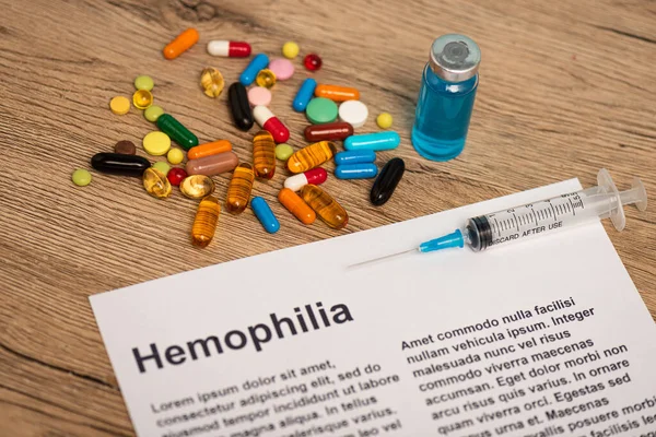 Selective focus of paper with hemophilia lettering near syringe, jar of vaccine and pills on wooden surface — Stock Photo