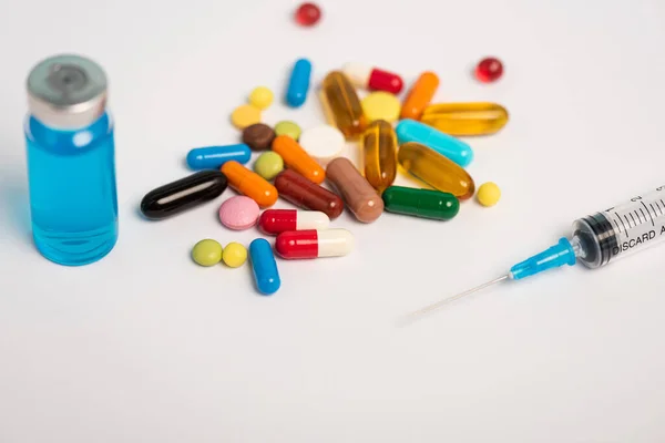 Close up view of colorful pills, syringe and jar of vaccine on white surface — Stock Photo