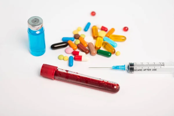 Tubo de ensayo con muestra de sangre, pastillas y jeringa con vacuna sobre fondo blanco - foto de stock