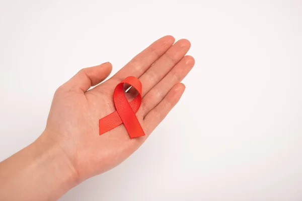 Cropped view of aids awareness red ribbon on female hand on white background — Stock Photo