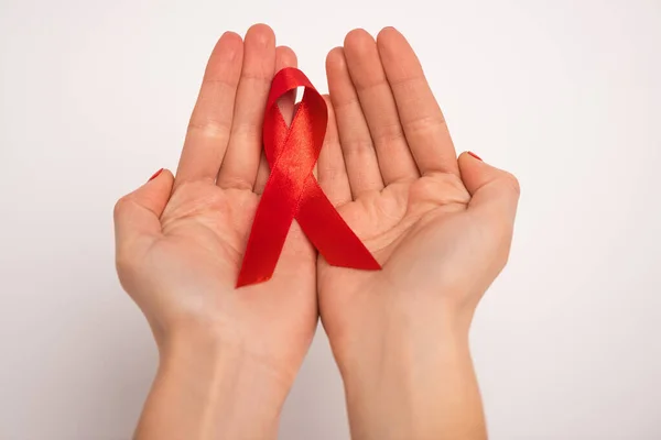 Vista recortada de la mujer sosteniendo cinta roja de SIDA conciencia sobre fondo blanco - foto de stock