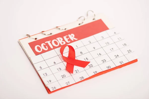 Focus selettivo del nastro rosso di sensibilizzazione aiuti sul calendario di ottobre isolato su bianco — Foto stock