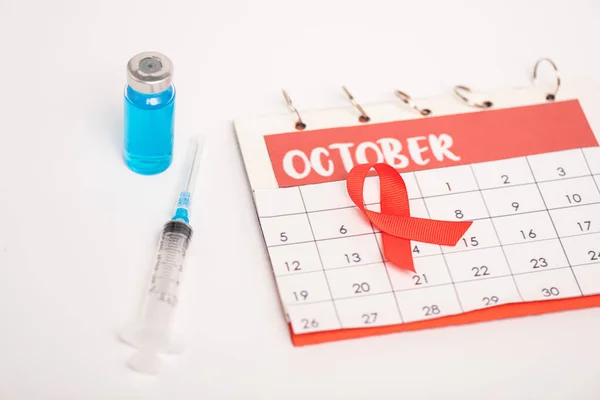 Enfoque selectivo del calendario con mes de octubre, ayuda a la conciencia cinta roja con jeringa en la superficie blanca - foto de stock