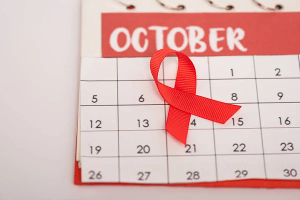 Vue rapprochée du ruban rouge de sensibilisation aux aides sur calendrier avec mois d'octobre isolé sur gris — Photo de stock