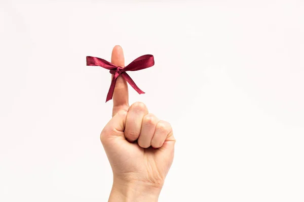 Cropped view of burgundy ribbon with bow on finger of woman isolated on white — Stock Photo