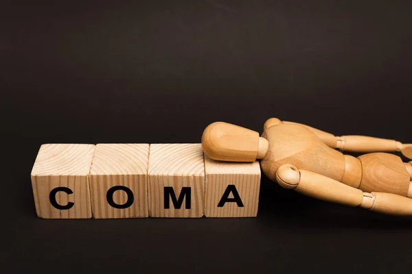 Wooden doll on cubes with coma lettering isolated on black — Stock Photo