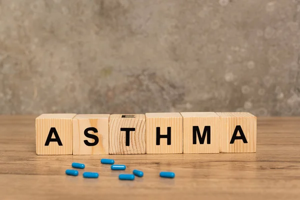 Selective focus of wooden cubes with asthma lettering and pills on wooden table on grey background — Stock Photo