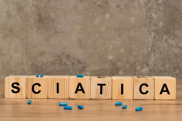 Selective focus of sciatica lettering on cubes with pills on wooden table on grey background — Stock Photo
