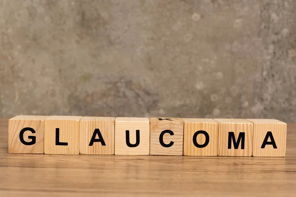 Letras em glaucoma sobre cubos sobre mesa de madeira sobre fundo cinza — Fotografia de Stock