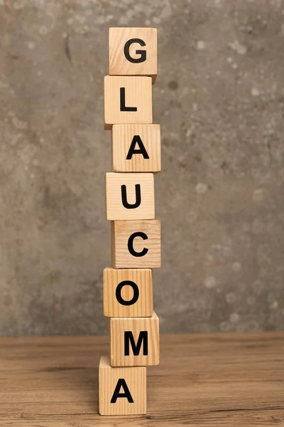 Cubos apilados con letras de glaucoma sobre mesa de madera sobre fondo gris - foto de stock