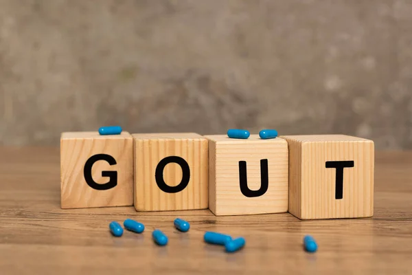 Selective focus of pills on wooden cubes with gout lettering on wooden table on grey background — Stock Photo