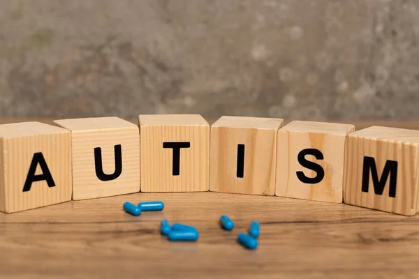 Foco seletivo de pílulas e blocos com letras de autismo na mesa de madeira em fundo cinza — Fotografia de Stock