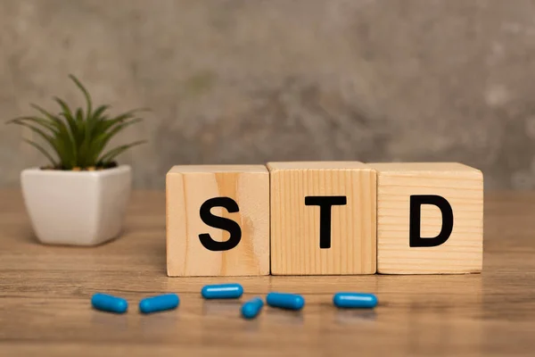 Mise au point sélective de blocs avec des lettres std, des pilules et des plantes sur une table en bois sur fond gris — Photo de stock