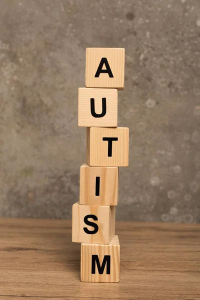 Blocos empilhados com letras autismo na mesa de madeira sobre fundo cinza texturizado — Fotografia de Stock