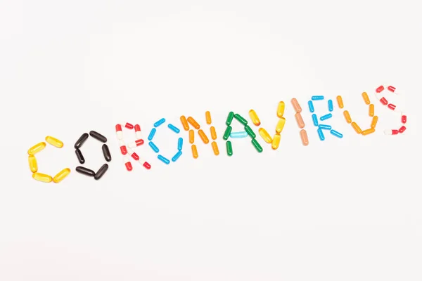 Visão superior de letras coronavírus de pílulas coloridas isoladas em branco — Fotografia de Stock