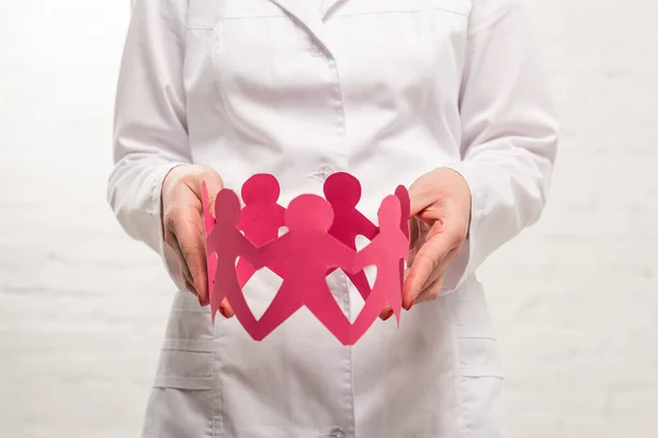 Cropped view of doctor holding paper figures of people on white background — Stock Photo