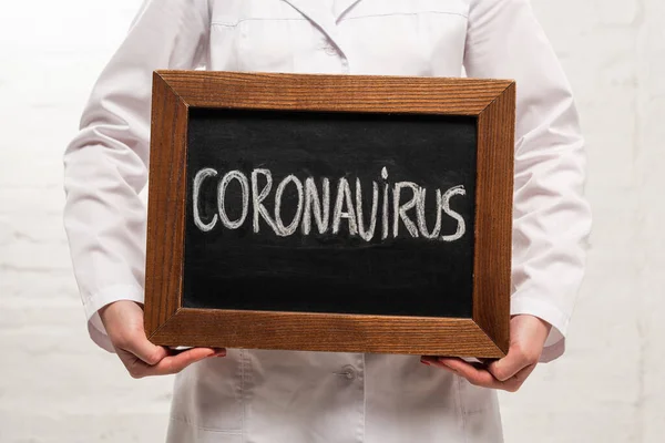 Обрезанный вид доктора, держащего доску с коронавирусной надписью на белом фоне — стоковое фото