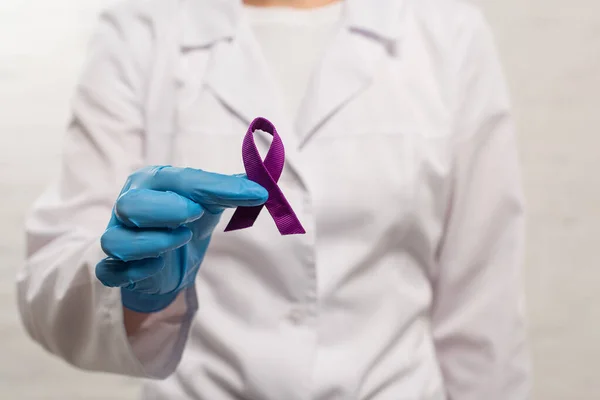 Focus selettivo del medico che tiene il nastro viola su sfondo bianco — Foto stock