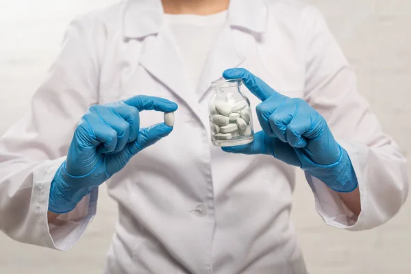 Vista recortada del médico sosteniendo frasco y píldora sobre fondo blanco - foto de stock
