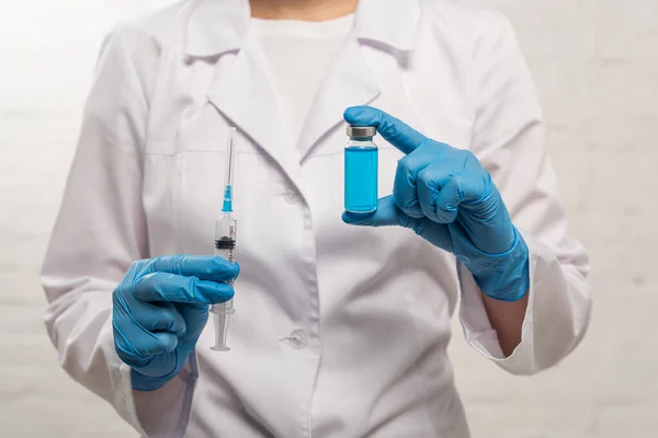 Vista recortada del médico que sostiene la jeringa y el frasco de vacuna sobre fondo blanco - foto de stock