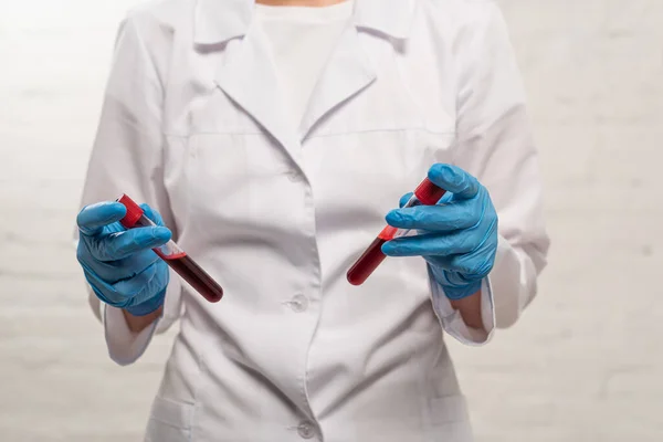 Vista recortada del médico sosteniendo tubos de ensayo con muestras de sangre sobre fondo blanco - foto de stock