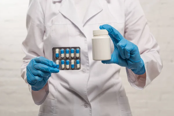 Cropped view of doctor holding jar and blister with pills on white background — Stock Photo