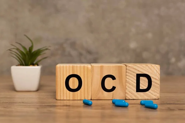 Focus selettivo di lettere ocd su cubi vicino pillole e pianta su superficie di legno su sfondo grigio — Foto stock