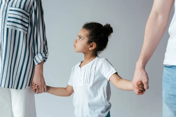 Сумна афроамериканська дитина тримає руки з розлученими прийомними батьками ізольовані на сірому — стокове фото