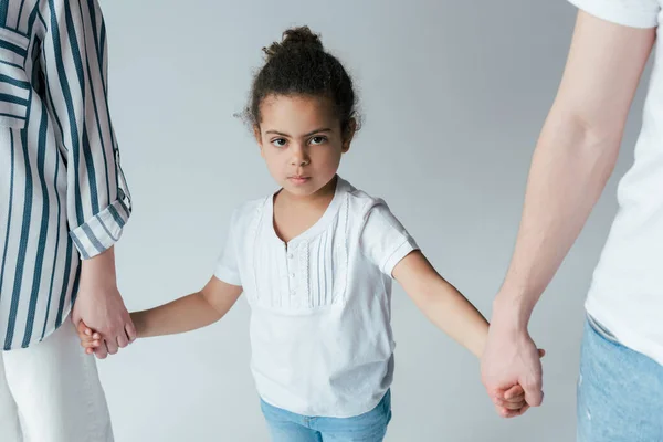 Niño afroamericano adoptado cogido de la mano con padres divorciados aislados en gris - foto de stock