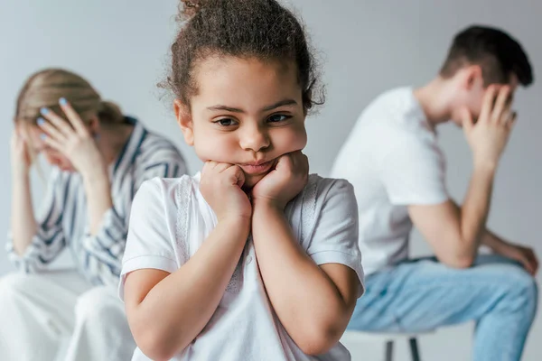 Enfoque selectivo de niño afroamericano triste tocar la cara cerca de padres adoptivos divorciados aislados en gris - foto de stock