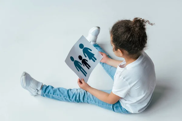 Vue aérienne d'un enfant afro-américain bouclé tenant du papier avec une famille dessinée sur blanc, concept d'adoption — Photo de stock