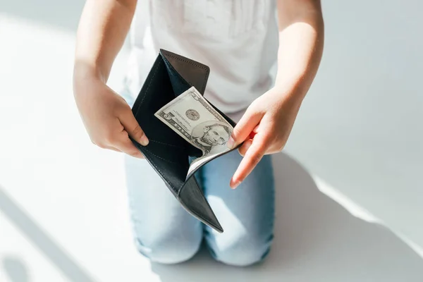 Vista recortada de niño sosteniendo billetera con billetes de dólar en concepto de pensión alimenticia blanca - foto de stock