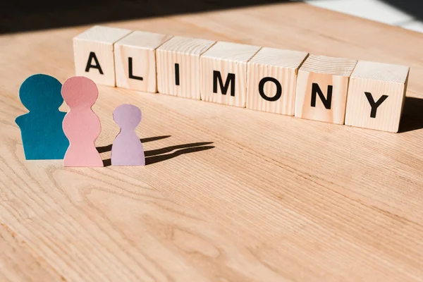 Wooden blocks with alimony lettering near family paper people on textured surface — Stock Photo