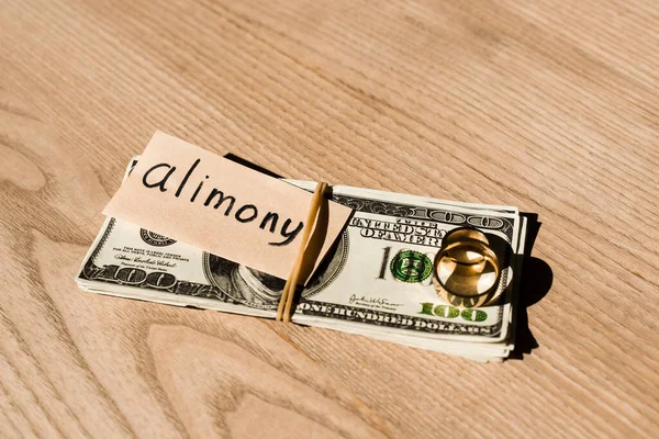 Paper with alimony lettering on dollar banknotes near engagement rings — Stock Photo