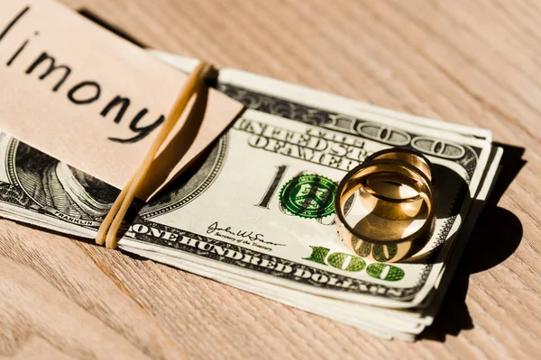 Messa a fuoco selettiva della carta con iscrizione sulle banconote in dollari vicino agli anelli di fidanzamento — Foto stock