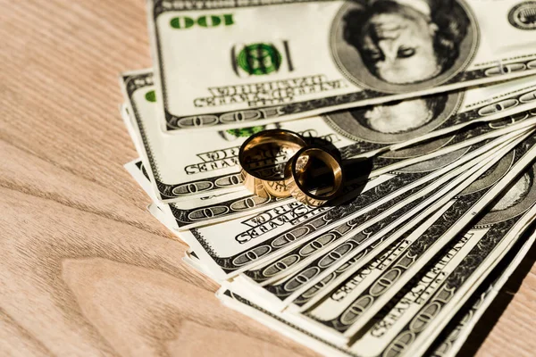 Dollar banknotes near golden engagement rings on wooden surface — Stock Photo